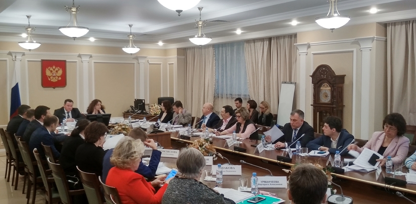 Цветное фото. Зал Министерства труда и социальной защиты Российской Федерации. Заседание, на котором присутствуют несколько десятков человек, сидящих вокруг овального стола в центре зала.